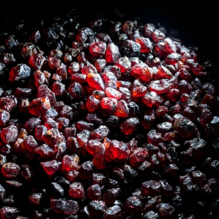 A bulk parcel of rough red garnet on a black background, hundreds of small stones ranging from bright red to deep purplish red